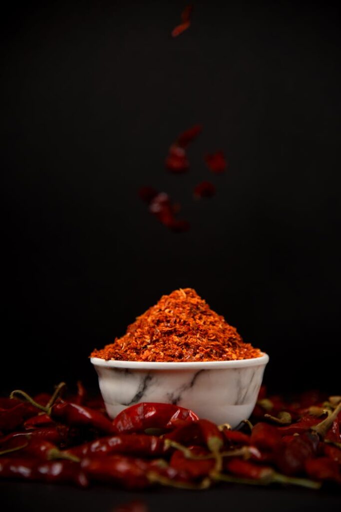 Red chili powder in a marble bowl with dried chilies on black background.