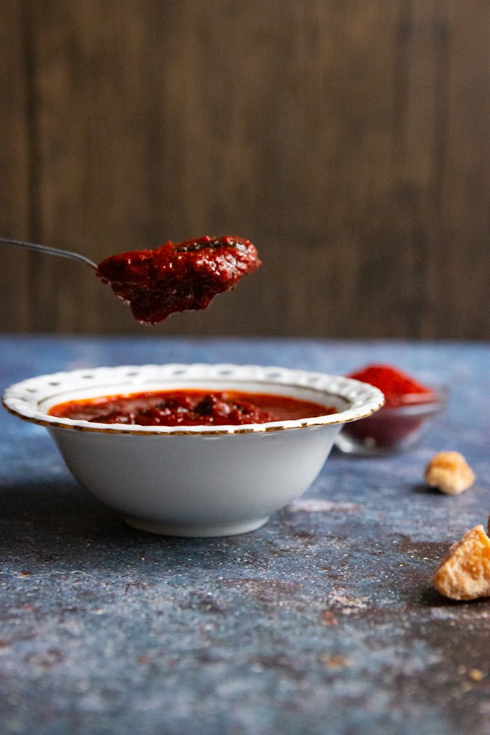 Close-up of a spicy red sauce in a bowl with a spoonful lifting the condiment, showcasing its texture.